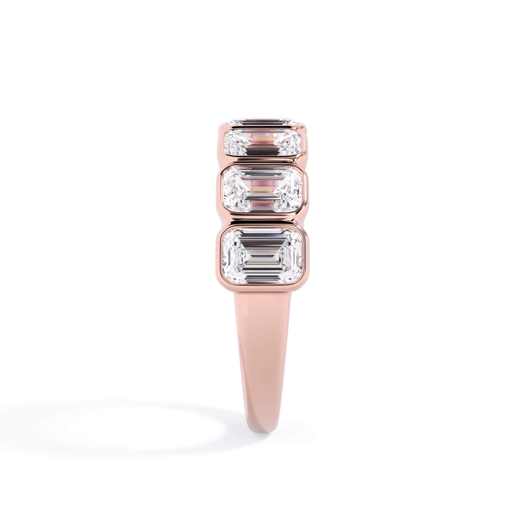 A picture of a seven stone diamond wedding ring with emerald cut diamonds that are bezel set in rose gold on a white background with a side profile view.