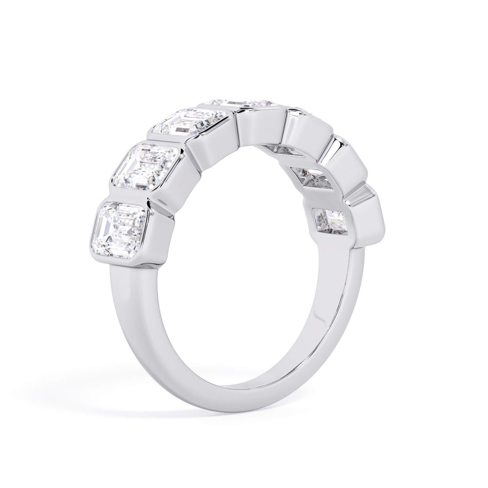 A picture of a seven stone diamond wedding ring with emerald cut diamonds that are bezel set in white gold or platinum on a white background with a slightly angled, through the finger view.