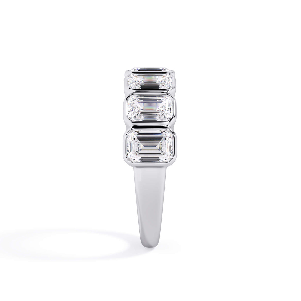A picture of a seven stone diamond wedding ring with emerald cut diamonds that are bezel set in white gold or platinum on a white background with a side profile view.