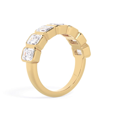 A picture of a seven stone diamond wedding ring with emerald cut diamonds that are bezel set in yellow gold on a white background with a slightly angled, through the finger view.