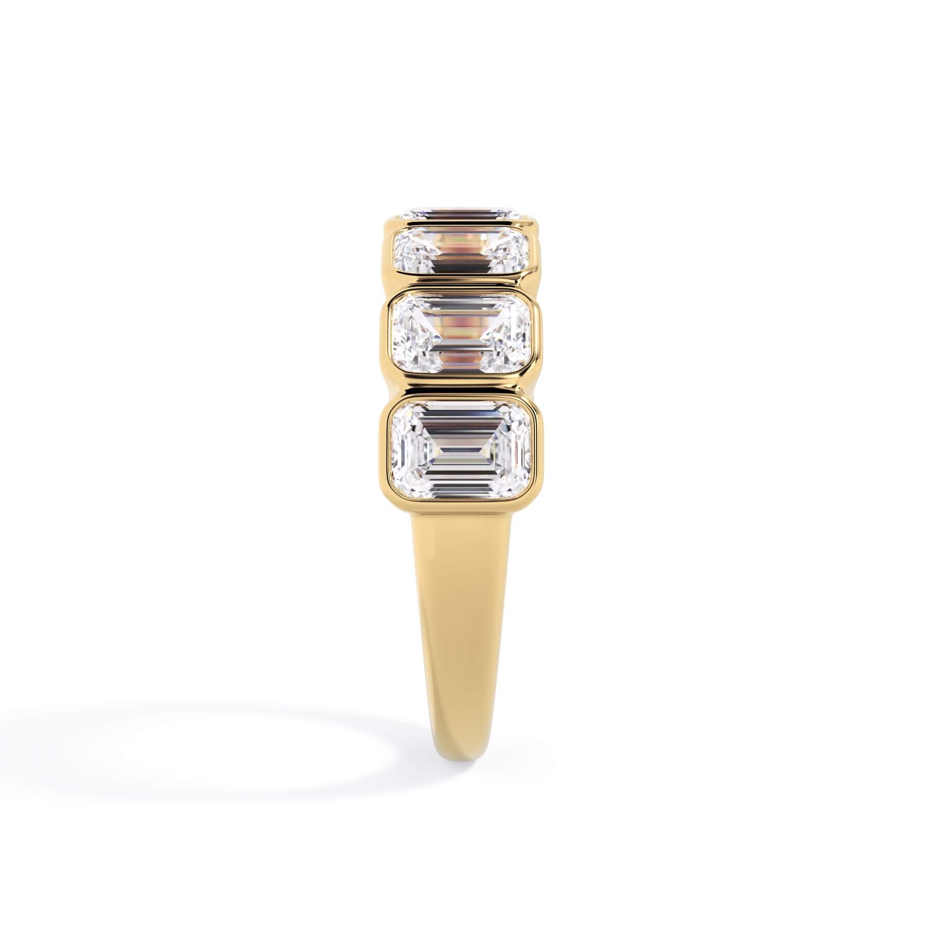 A picture of a seven stone diamond wedding ring with emerald cut diamonds that are bezel set in yellow gold on a white background with a side profile view.