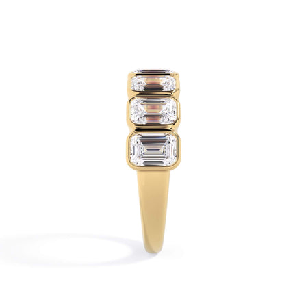 A picture of a seven stone diamond wedding ring with emerald cut diamonds that are bezel set in yellow gold on a white background with a side profile view.