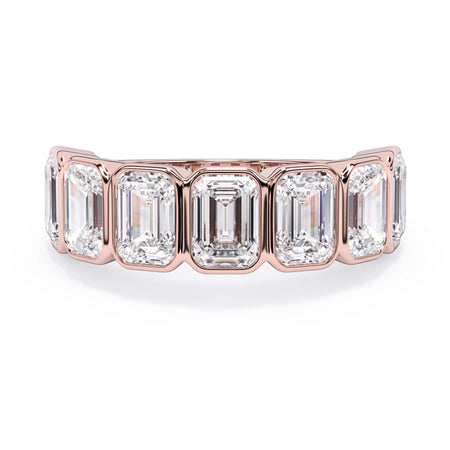 A picture of a seven stone diamond wedding ring with emerald cut diamonds that are bezel set in rose gold on a white background with the ring facing forward, lying down.
