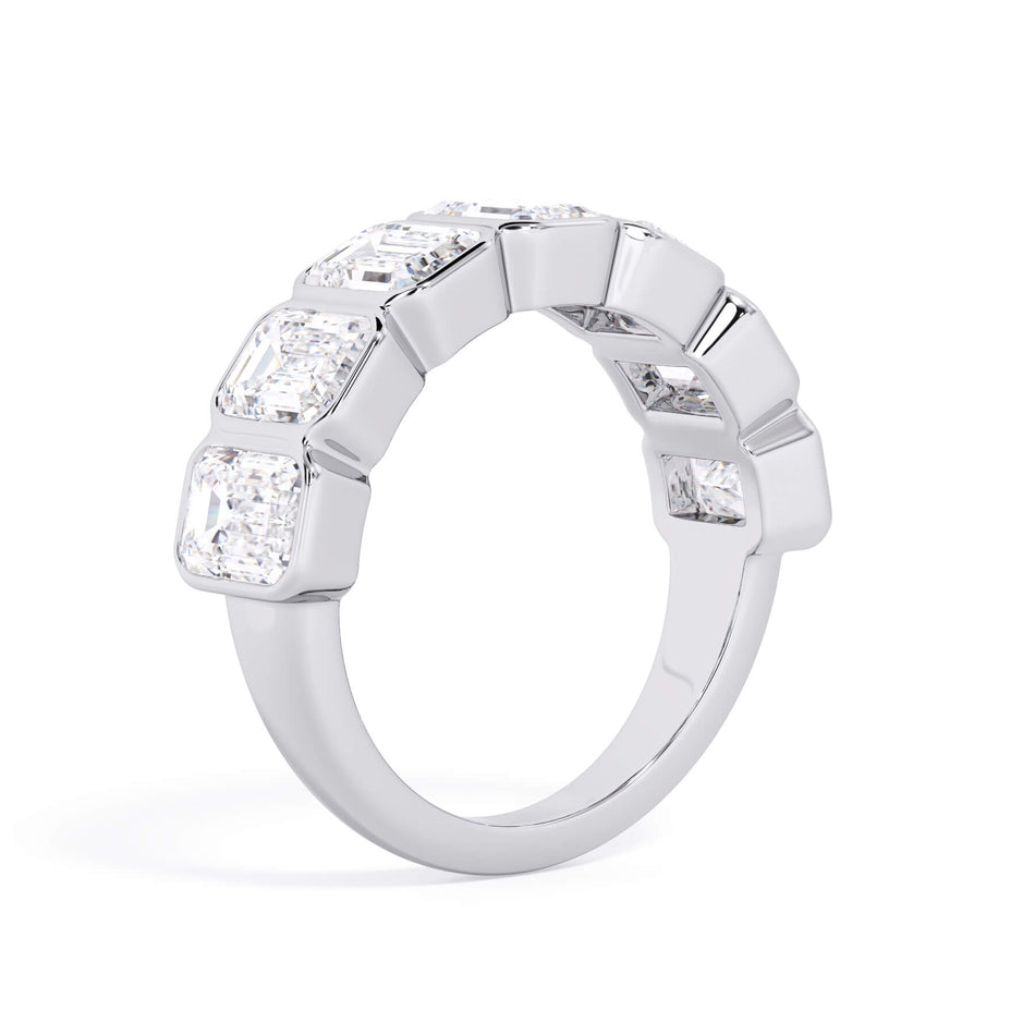 A picture of a seven stone diamond wedding ring with emerald cut diamonds that are bezel set in white gold or platinum on a white background with a slightly angled, through the finger view.