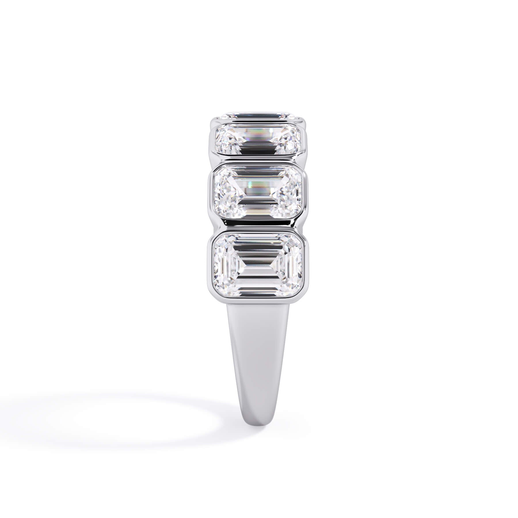 A picture of a seven stone diamond wedding ring with emerald cut diamonds that are bezel set in white gold or platinum on a white background with a side profile view.