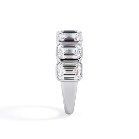 A picture of a seven stone diamond wedding ring with emerald cut diamonds that are bezel set in white gold or platinum on a white background with a side profile view.