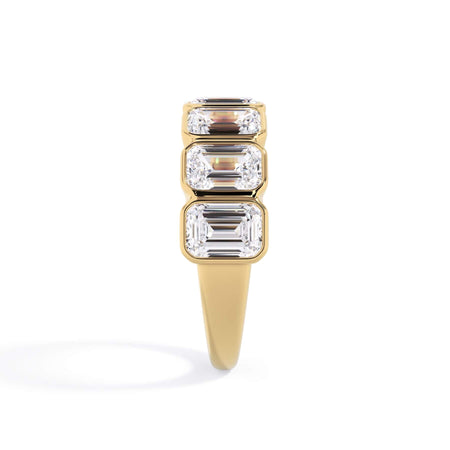 A picture of a seven stone diamond wedding ring with emerald cut diamonds that are bezel set in yellow gold on a white background with a side profile view.