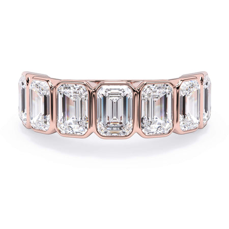 A picture of a seven stone diamond wedding ring with emerald cut diamonds that are bezel set in rose gold on a white background with the ring facing forward, lying down.