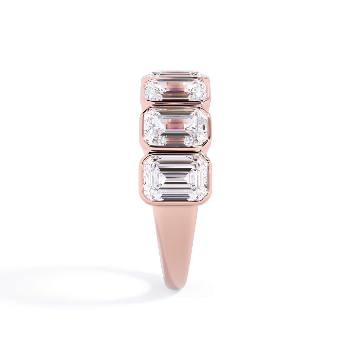 A picture of a seven stone diamond wedding ring with emerald cut diamonds that are bezel set in rose gold on a white background with a side profile view.