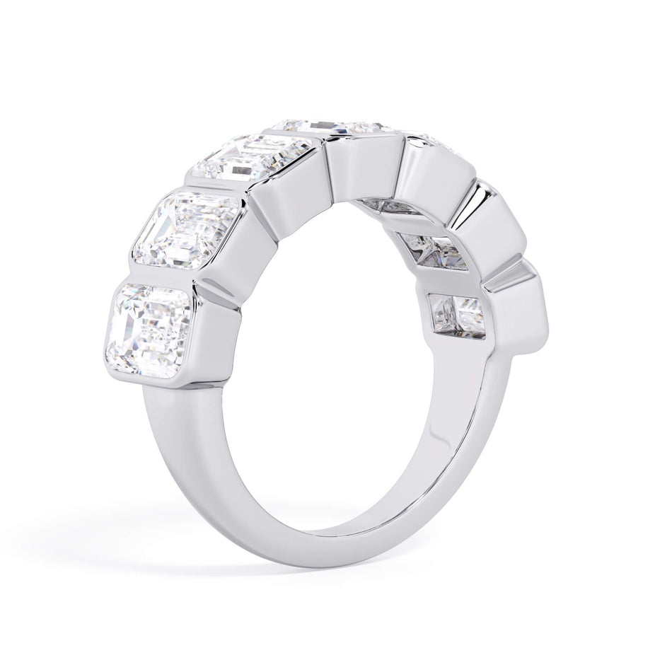 A picture of a seven stone diamond wedding ring with emerald cut diamonds that are bezel set in white gold or platinum on a white background with a slightly angled, through the finger view.