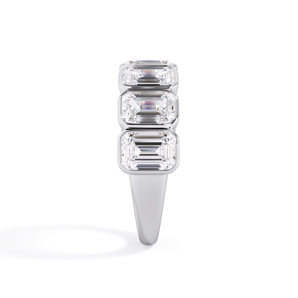 A picture of a seven stone diamond wedding ring with emerald cut diamonds that are bezel set in white gold or platinum on a white background with a side profile view.