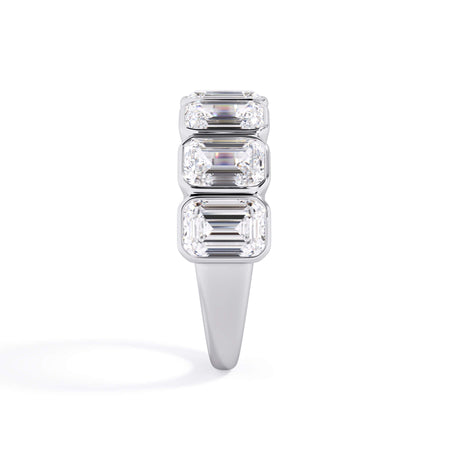 A picture of a seven stone diamond wedding ring with emerald cut diamonds that are bezel set in white gold or platinum on a white background with a side profile view.