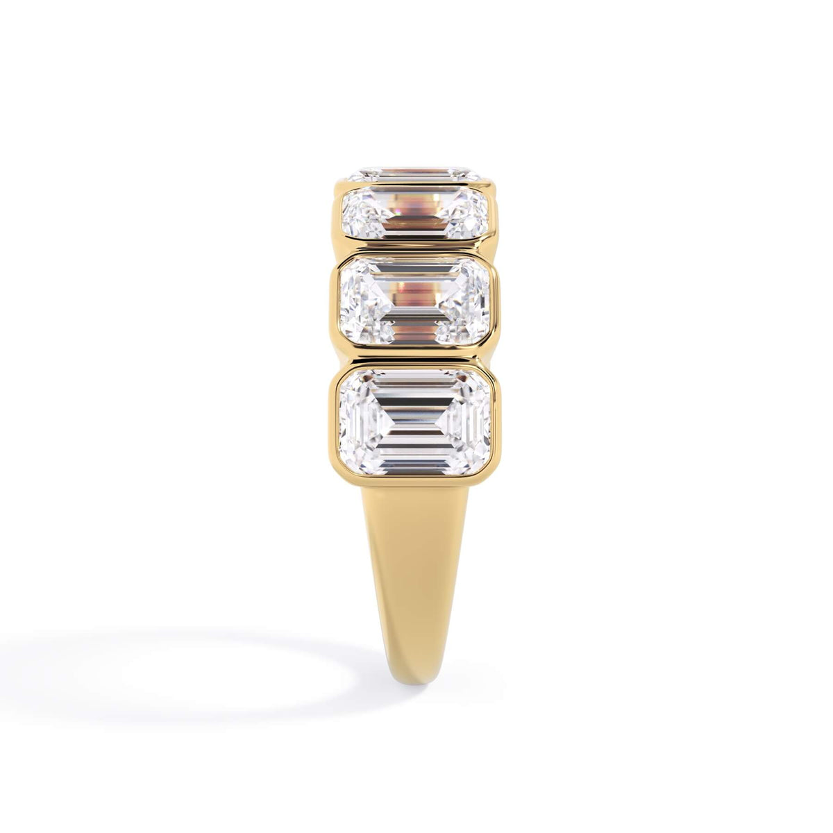 A picture of a seven stone diamond wedding ring with emerald cut diamonds that are bezel set in yellow gold on a white background with a side profile view.