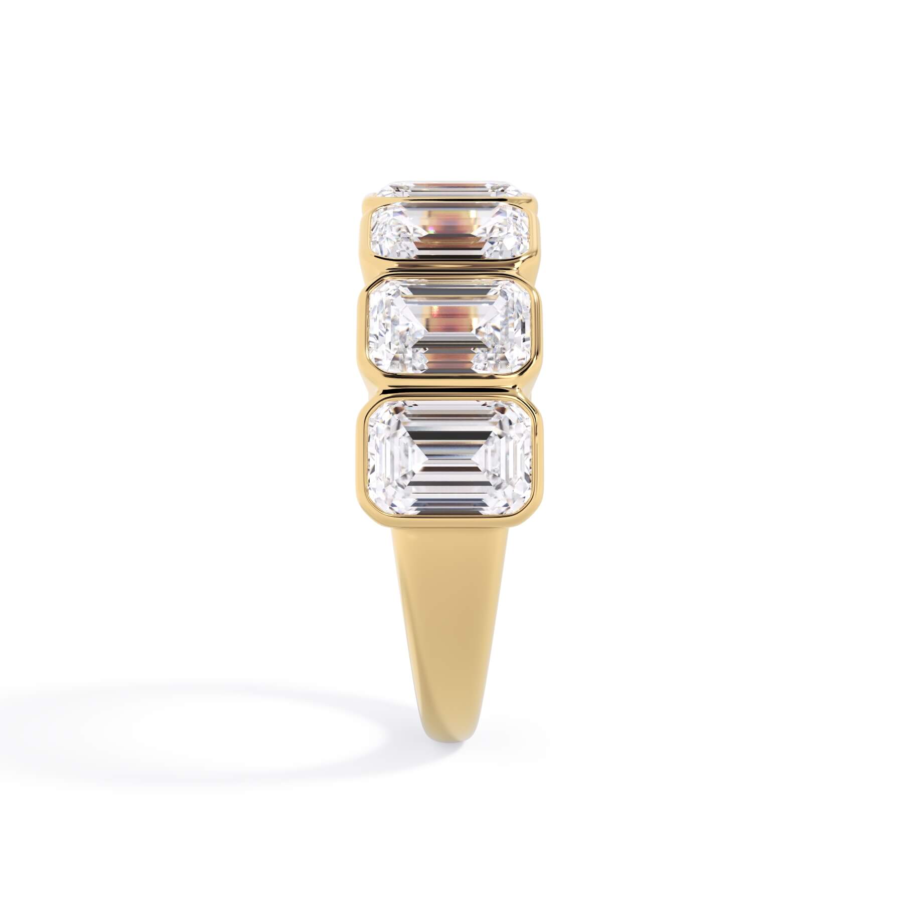 A picture of a seven stone diamond wedding ring with emerald cut diamonds that are bezel set in yellow gold on a white background with a side profile view.