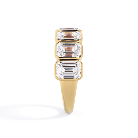 A picture of a seven stone diamond wedding ring with emerald cut diamonds that are bezel set in yellow gold on a white background with a side profile view.