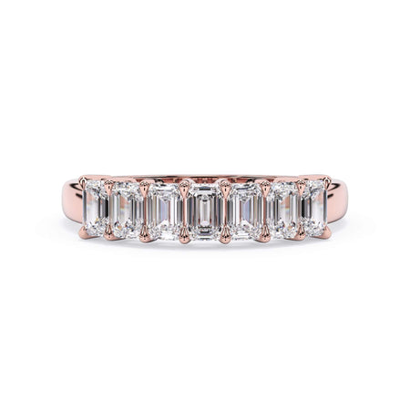 A picture of a seven stone diamond wedding ring with emerald cut diamonds that are shared prong set in rose gold on a white background with the ring facing forward, lying down.