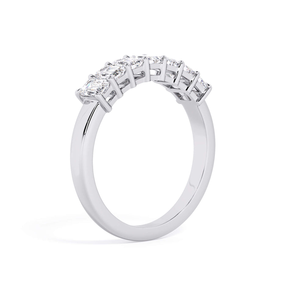 A picture of a seven stone diamond wedding ring with emerald cut diamonds that are shared prong set in white gold or platinum on a white background with a slightly angled, through the finger view.