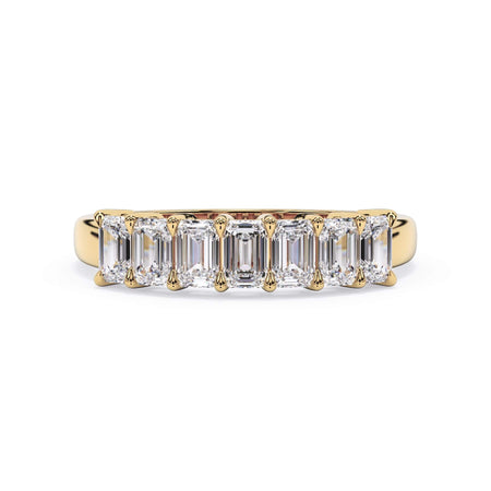 A picture of a seven stone diamond wedding ring with emerald cut diamonds that are shared prong set in yellow gold on a white background with the ring facing forward, lying down.