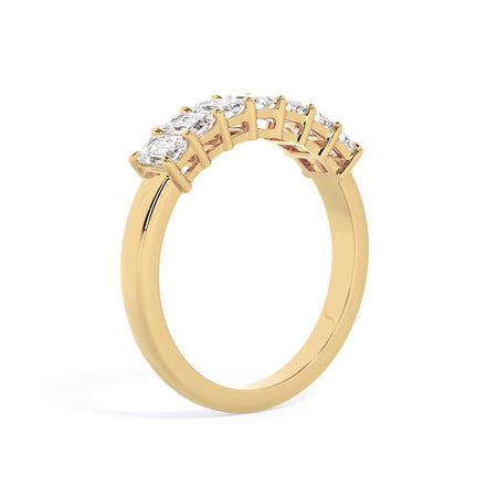 A picture of a seven stone diamond wedding ring with emerald cut diamonds that are shared prong set in yellow gold on a white background with a slightly angled, through the finger view.