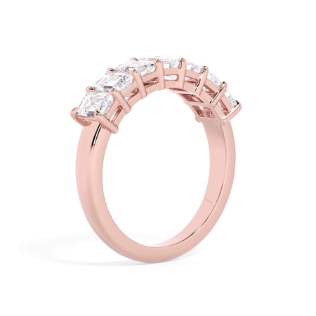 A picture of a seven stone diamond wedding ring with emerald cut diamonds that are shared prong set in rose gold on a white background with a slightly angled, through the finger view.