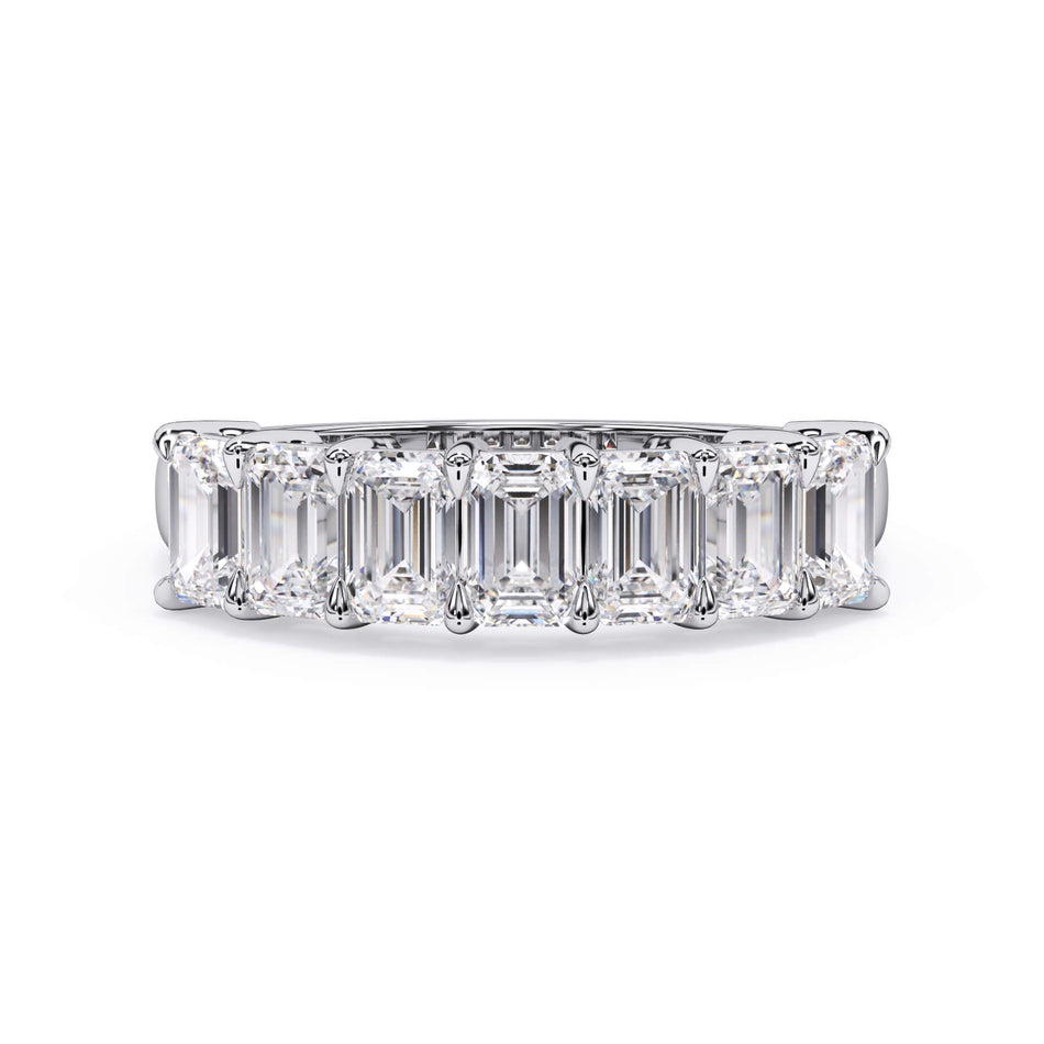 A picture of a seven stone diamond wedding ring with emerald cut diamonds that are shared prong set in white gold or platinum on a white background with the ring facing forward, lying down.
