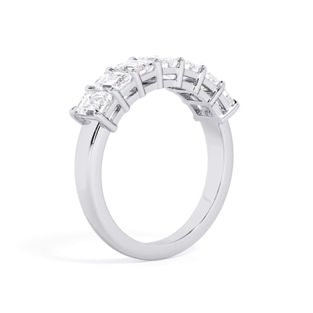 A picture of a seven stone diamond wedding ring with emerald cut diamonds that are shared prong set in white gold or platinum on a white background with a slightly angled, through the finger view.