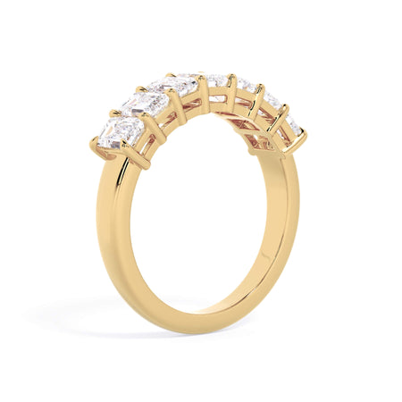A picture of a seven stone diamond wedding ring with emerald cut diamonds that are shared prong set in yellow gold on a white background with a slightly angled, through the finger view.