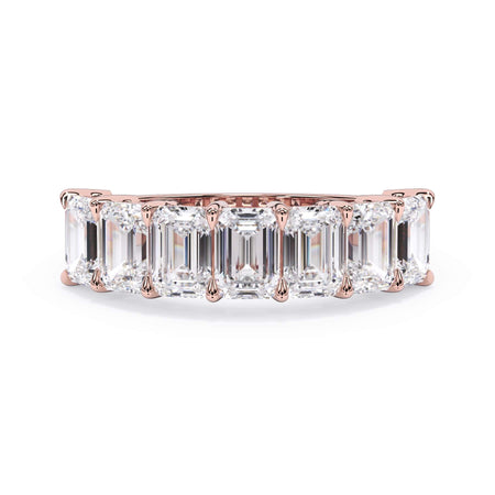 A picture of a seven stone diamond wedding ring with emerald cut diamonds that are shared prong set in rose gold on a white background with the ring facing forward, lying down.