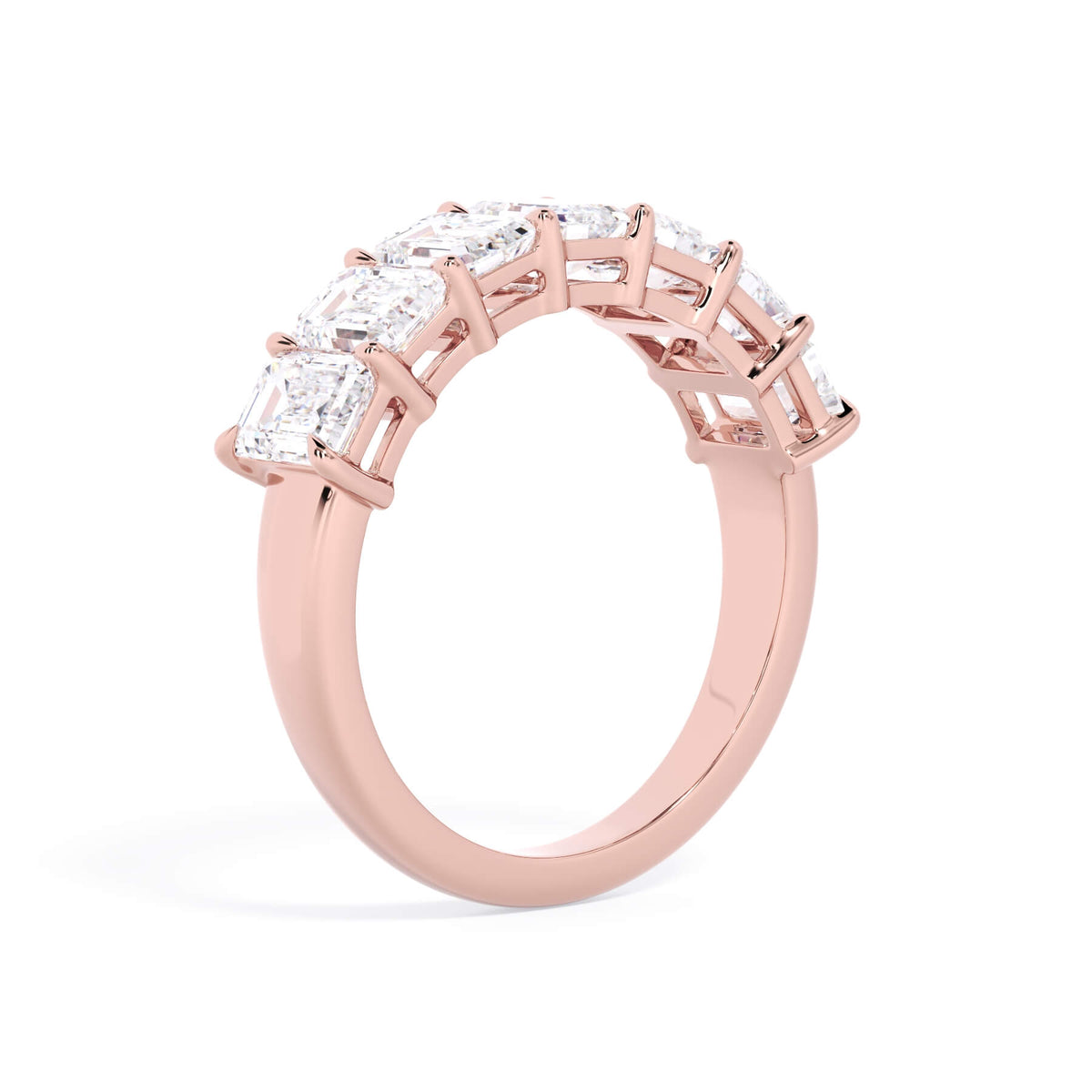 A picture of a seven stone diamond wedding ring with emerald cut diamonds that are shared prong set in rose gold on a white background with a slightly angled, through the finger view.