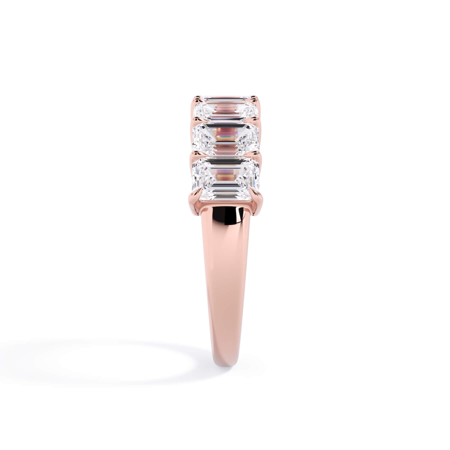A picture of a seven stone diamond wedding ring with emerald cut diamonds that are shared prong set in rose gold on a white background with a side profile view.