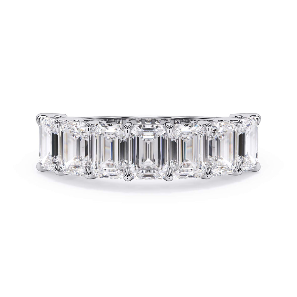 A picture of a seven stone diamond wedding ring with emerald cut diamonds that are shared prong set in white gold or platinum on a white background with the ring facing forward, lying down.