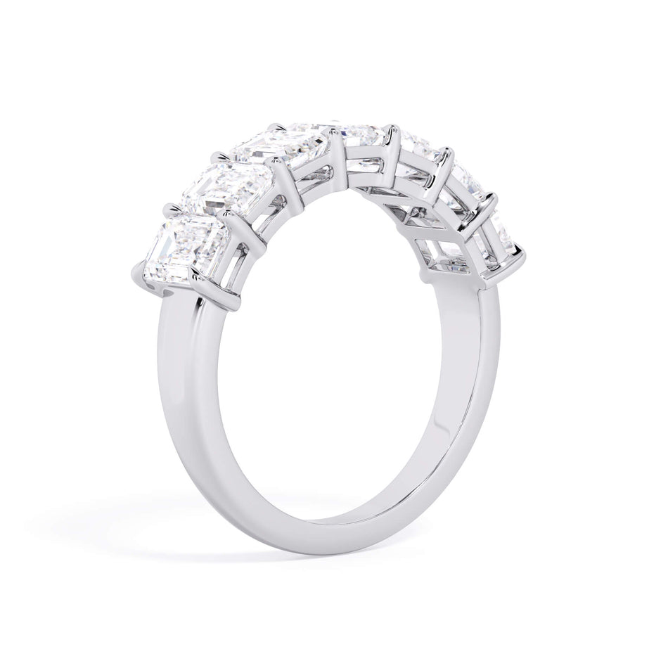 A picture of a seven stone diamond wedding ring with emerald cut diamonds that are shared prong set in white gold or platinum on a white background with a slightly angled, through the finger view.