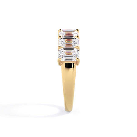 A picture of a seven stone diamond wedding ring with emerald cut diamonds that are shared prong set in yellow gold on a white background with a side profile view.