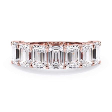 A picture of a seven stone diamond wedding ring with emerald cut diamonds that are shared prong set in rose gold on a white background with the ring facing forward, lying down.