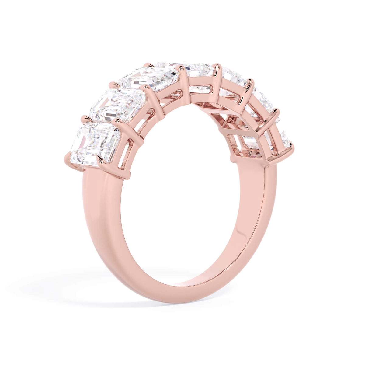 A picture of a seven stone diamond wedding ring with emerald cut diamonds that are shared prong set in rose gold on a white background with a slightly angled, through the finger view.