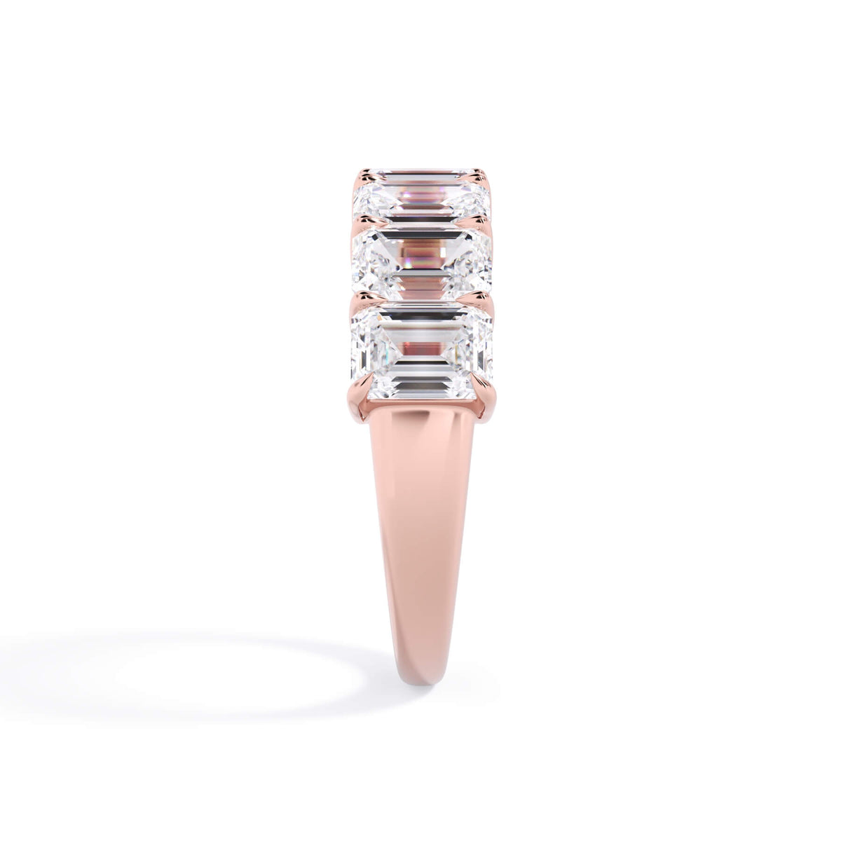A picture of a seven stone diamond wedding ring with emerald cut diamonds that are shared prong set in rose gold on a white background with a side profile view.