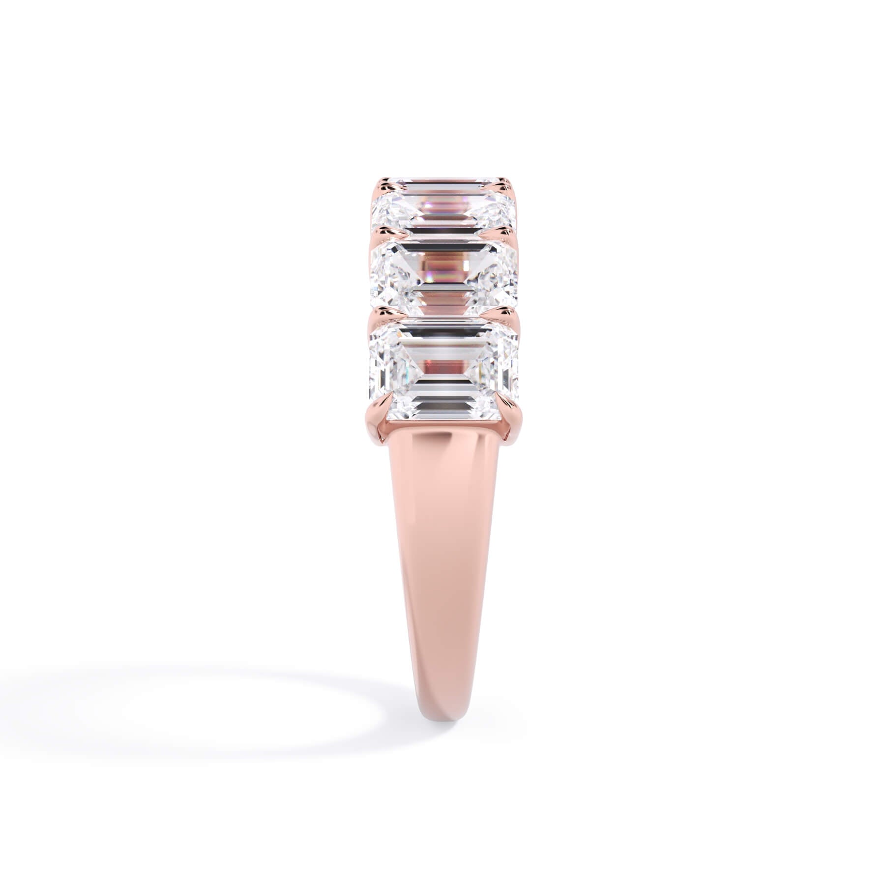A picture of a seven stone diamond wedding ring with emerald cut diamonds that are shared prong set in rose gold on a white background with a side profile view.