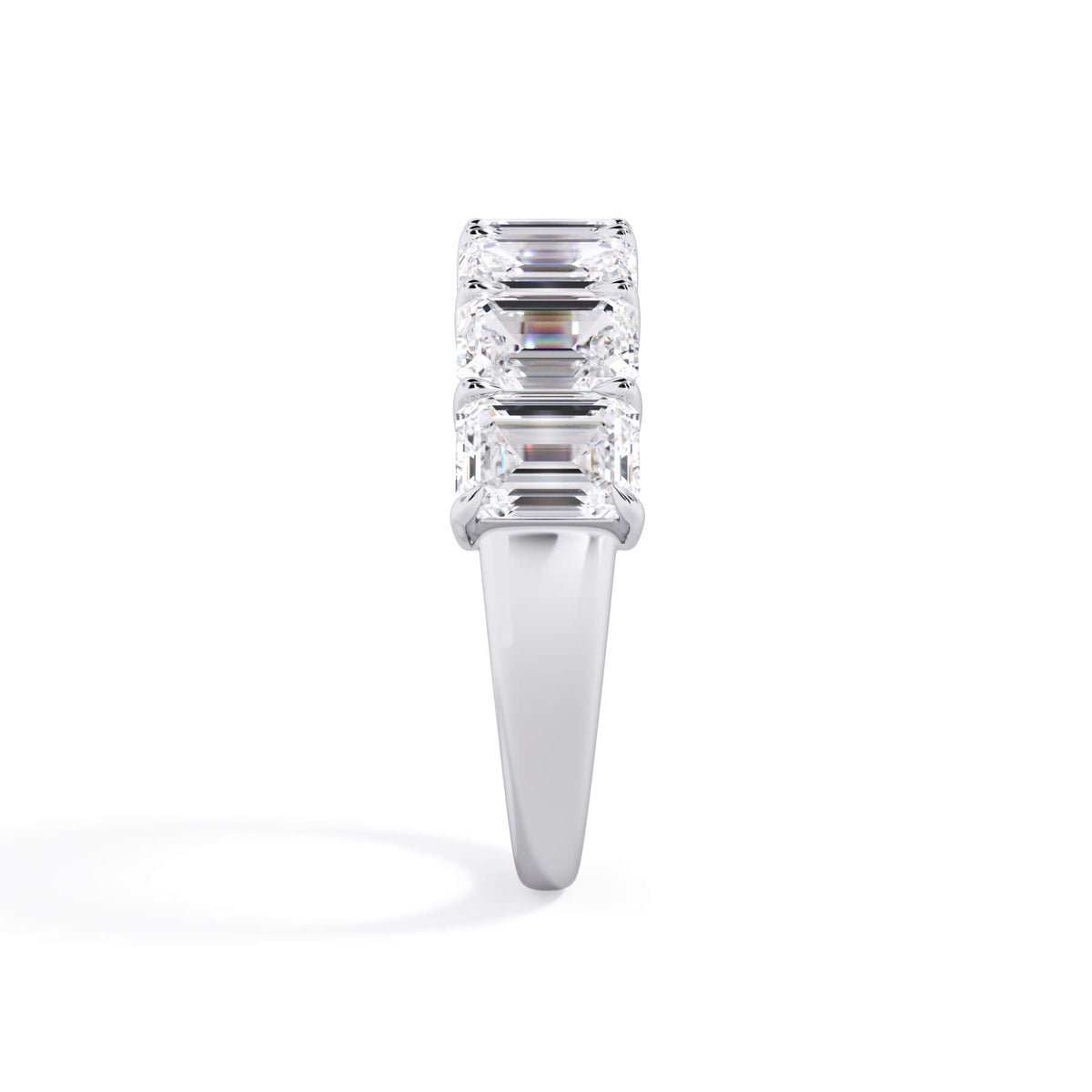 A picture of a seven stone diamond wedding ring with emerald cut diamonds that are shared prong set in white gold or platinum on a white background with a side profile view.