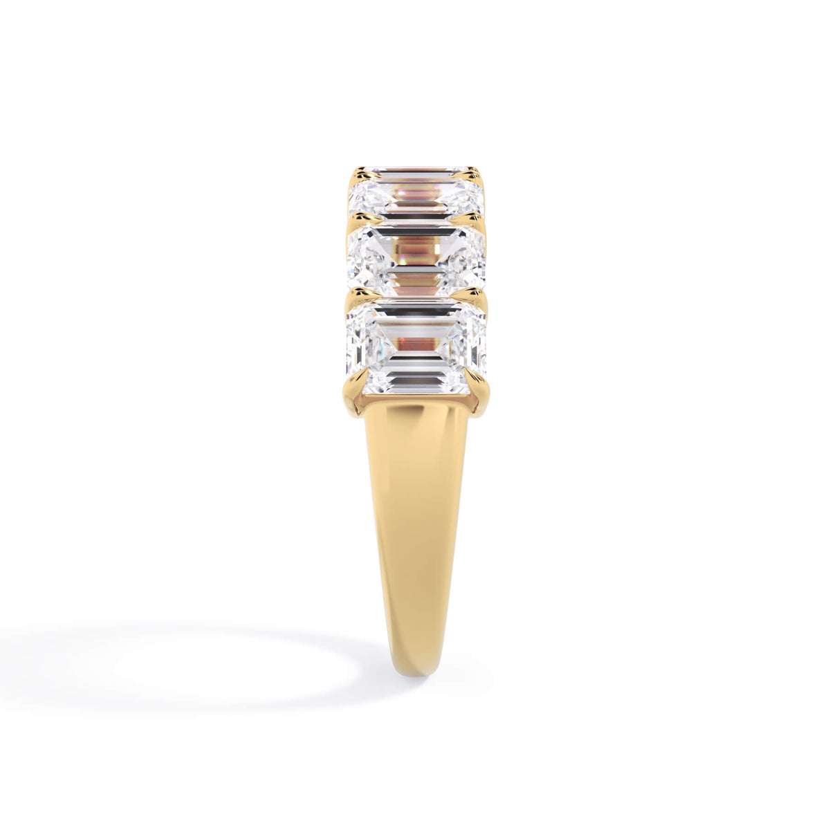A picture of a seven stone diamond wedding ring with emerald cut diamonds that are shared prong set in yellow gold on a white background with a side profile view.