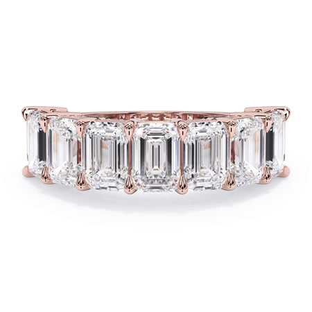 A picture of a seven stone diamond wedding ring with emerald cut diamonds that are shared prong set in rose gold on a white background with the ring facing forward, lying down.