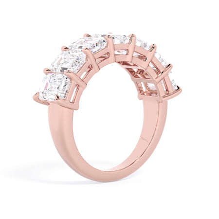 A picture of a seven stone diamond wedding ring with emerald cut diamonds that are shared prong set in rose gold on a white background with a slightly angled, through the finger view.
