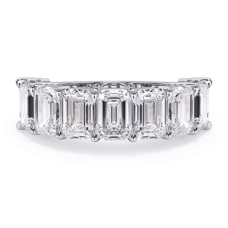 A picture of a seven stone diamond wedding ring with emerald cut diamonds that are shared prong set in white gold or platinum on a white background with the ring facing forward, lying down.