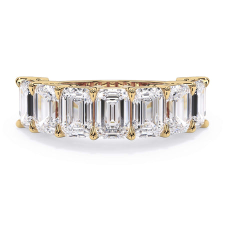 A picture of a seven stone diamond wedding ring with emerald cut diamonds that are shared prong set in yellow gold on a white background with the ring facing forward, lying down.