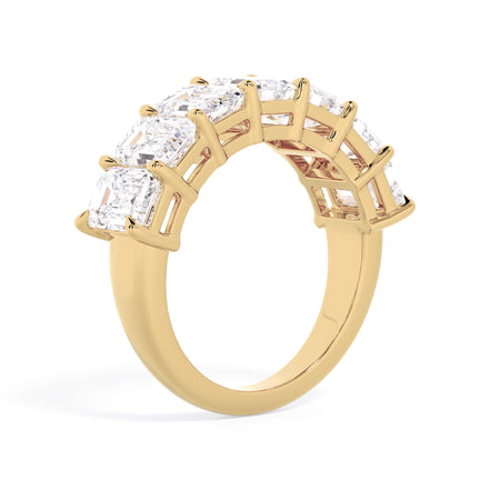 A picture of a seven stone diamond wedding ring with emerald cut diamonds that are shared prong set in yellow gold on a white background with a slightly angled, through the finger view.