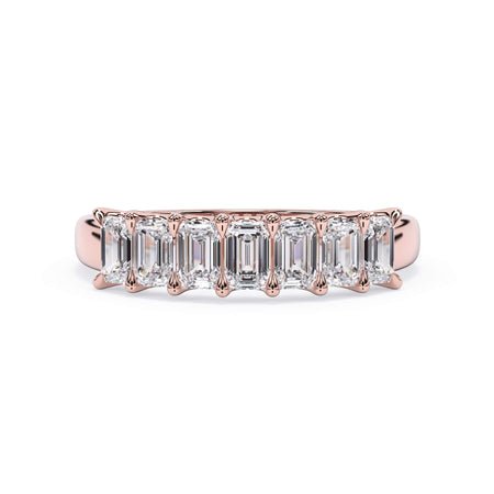 A picture of a seven stone diamond wedding ring with emerald cut diamonds that are U prong set in rose gold on a white background with the ring facing forward, lying down.
