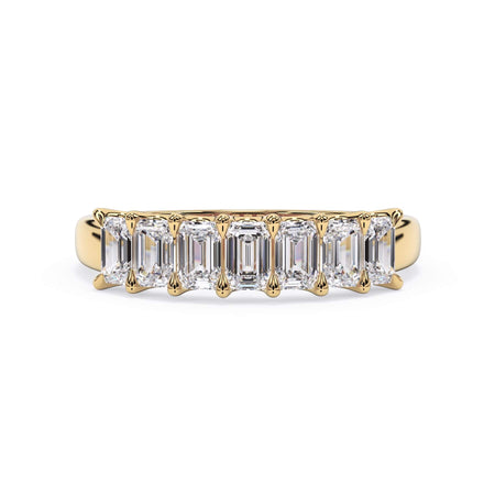 A picture of a seven stone diamond wedding ring with emerald cut diamonds that are U prong set in yellow gold on a white background with the ring facing forward, lying down.
