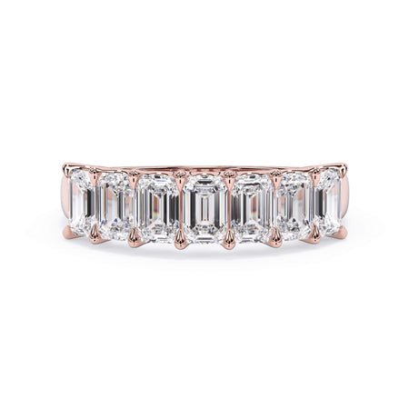 A picture of a seven stone diamond wedding ring with emerald cut diamonds that are U prong set in rose gold on a white background with the ring facing forward, lying down.