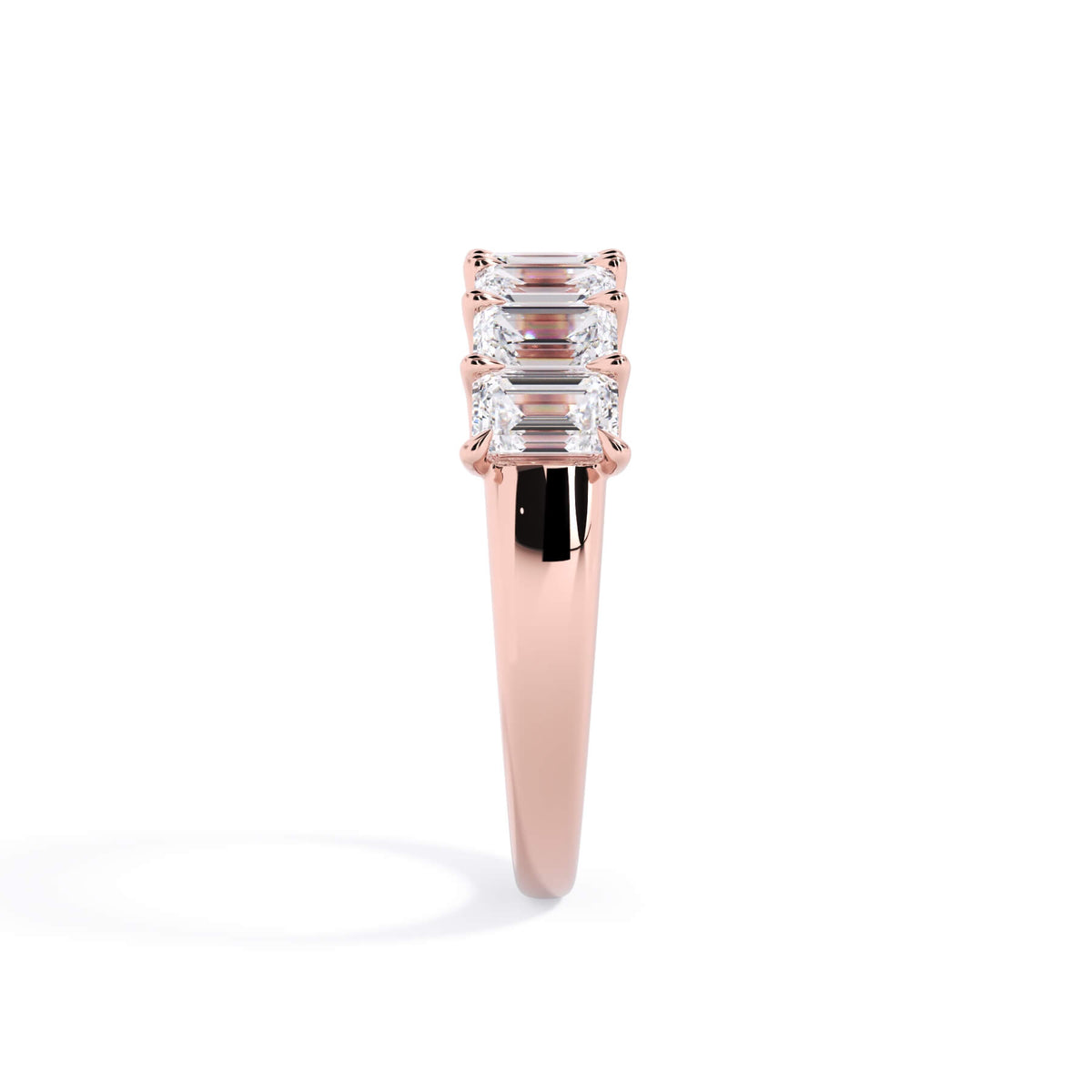 A picture of a seven stone diamond wedding ring with emerald cut diamonds that are U prong set in rose gold on a white background with a side profile view.