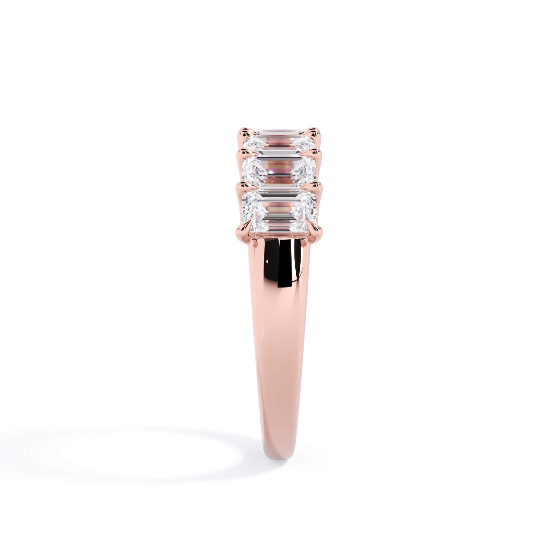 A picture of a seven stone diamond wedding ring with emerald cut diamonds that are U prong set in rose gold on a white background with a side profile view.
