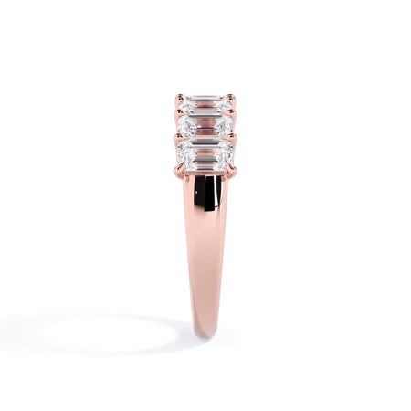 A picture of a seven stone diamond wedding ring with emerald cut diamonds that are U prong set in rose gold on a white background with a side profile view.